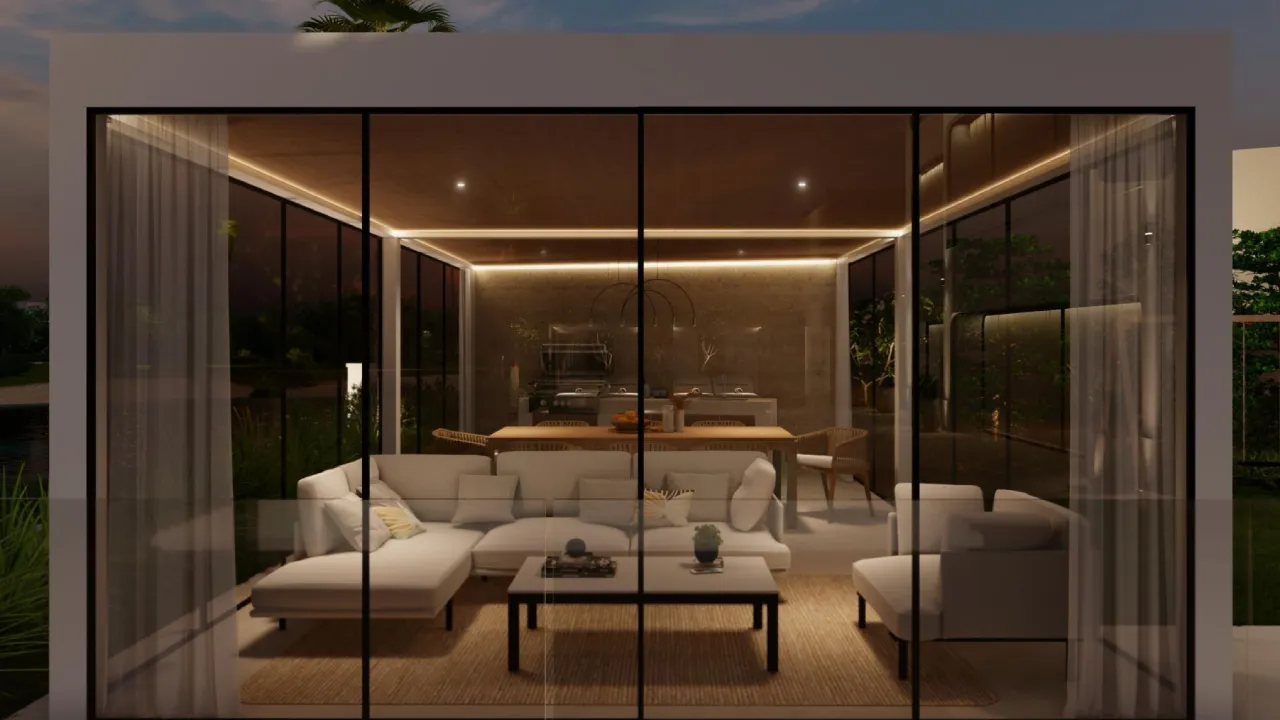 Modern glass room with lounge seating, dining area, backyard kitchen, floor-to-ceiling sliding doors, sheer curtains, and warm interior lighting at dusk.