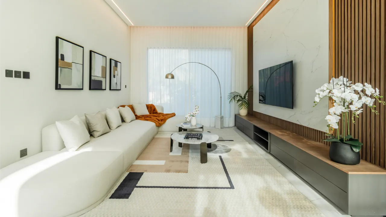 Modern living room with long sofa, TV wall, built-in storage, warm lighting, and renewed flooring