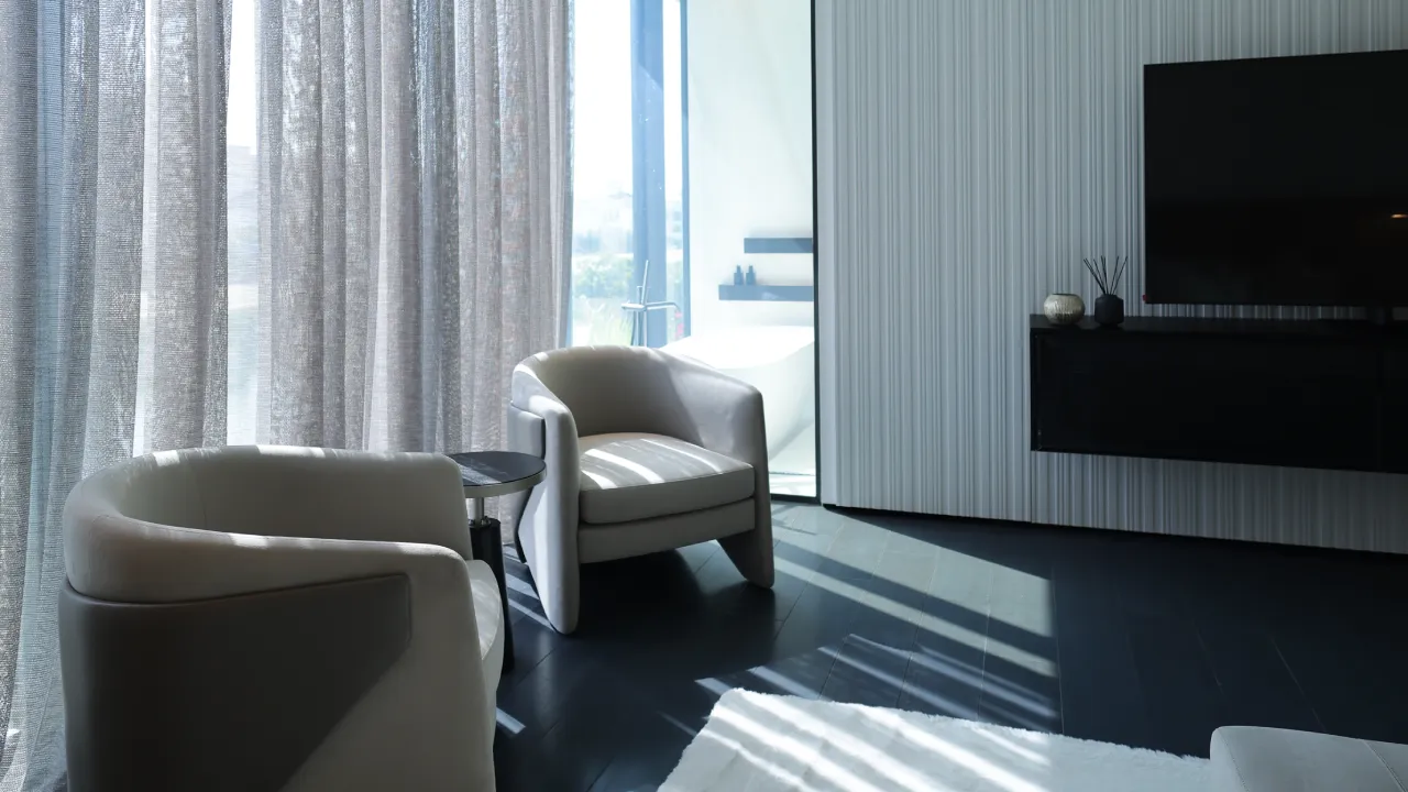 Bedroom sitting area after villa design in Palm Jumeirah with curved lounge chairs, sheer curtains, dark flooring, and a floating black media unit