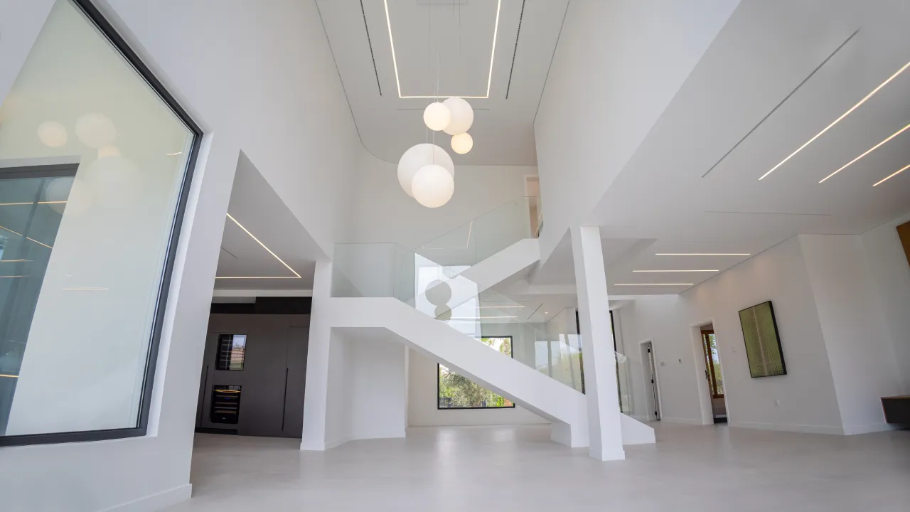 Dubai full home renovation with double-height interior, glass stair railing, white walls, large windows, and sculptural globe pendant lights