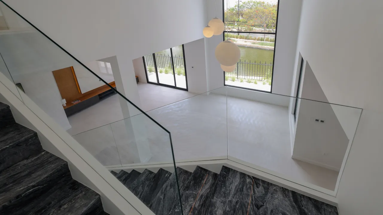 Dubai renovated villa double-height staircase with dark stone steps, glass railing, tall windows, and round pendant lights