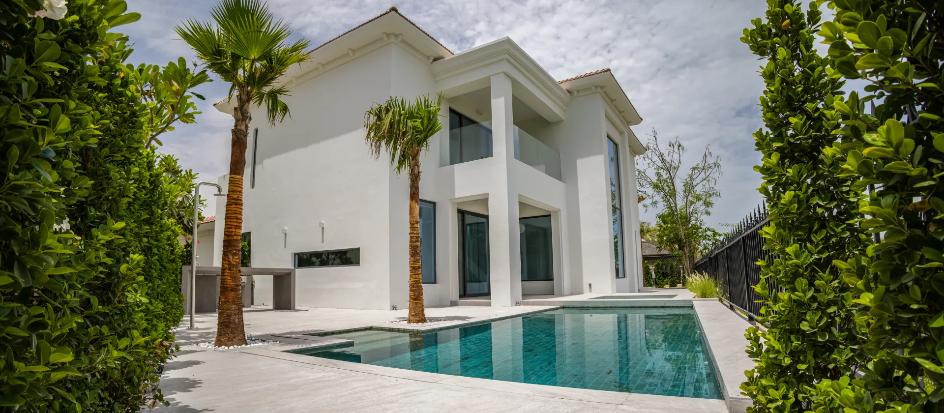 Dubai villa renovation exterior with white facade, glass balcony, black-framed windows, palms, pool terrace, and modern outdoor finishes