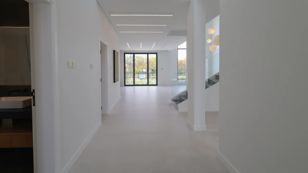Full home renovation ground floor with white walls, pale flooring, linear ceiling lights, glass staircase, and garden-facing windows