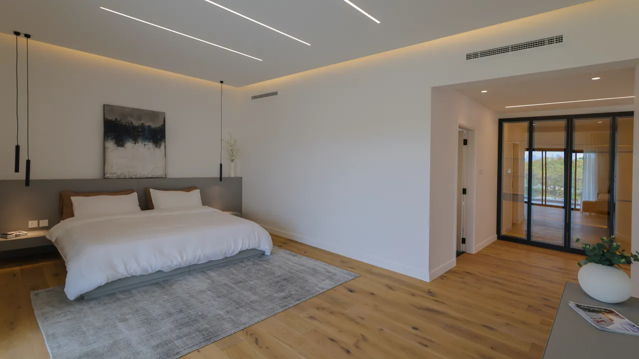 Jumeirah Islands bedroom design with wood flooring, white bedding, grey headboard wall, pendant lights, and soft modern finishes