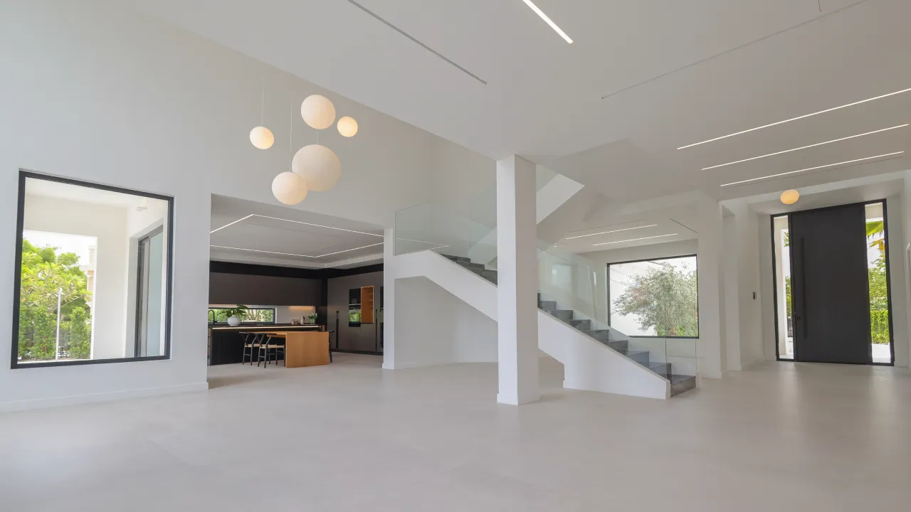 Jumeirah Islands renovated villa interior with open-plan ground floor, glass staircase, globe pendant lights, kitchen view, and black front door