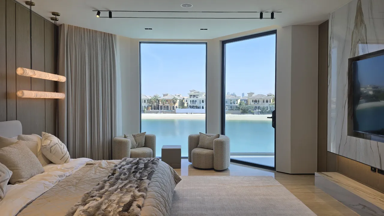 Luxury master bedroom renovation in Palm Jumeirah Dubai with waterfront windows, warm wood wall panels, marble TV wall and soft neutral furniture