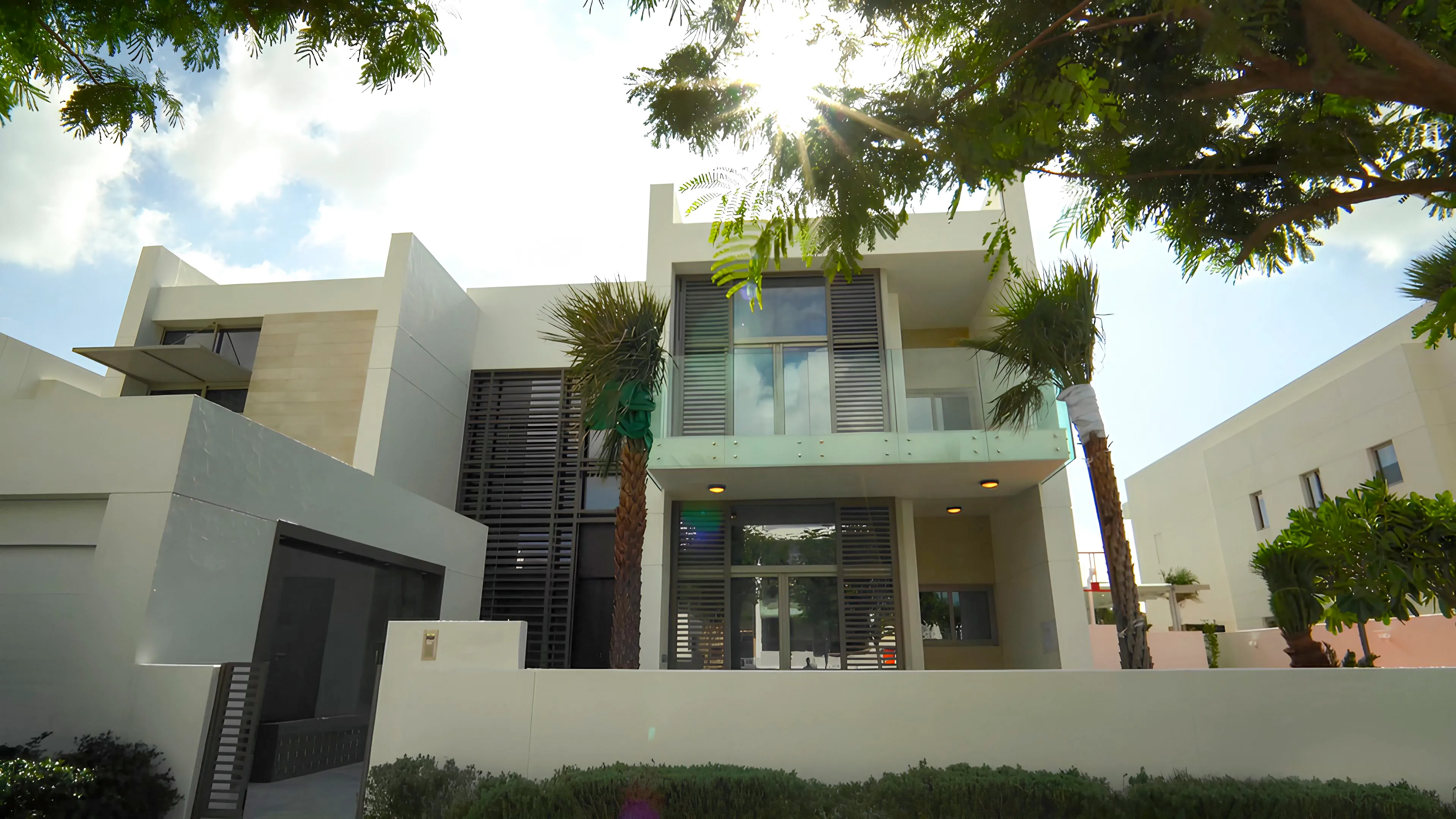 Front exterior of a luxury villa renovation in MBR District One Dubai with modern facade, glass balcony, palm trees, and dark privacy screens