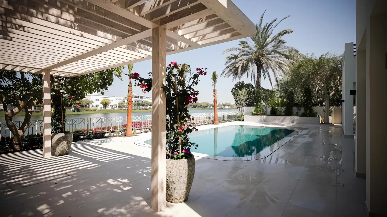 Backyard pool remodeling in Meadows Dubai with timber pergola, planting, terrace seating, lake view, and renewed villa facade.
