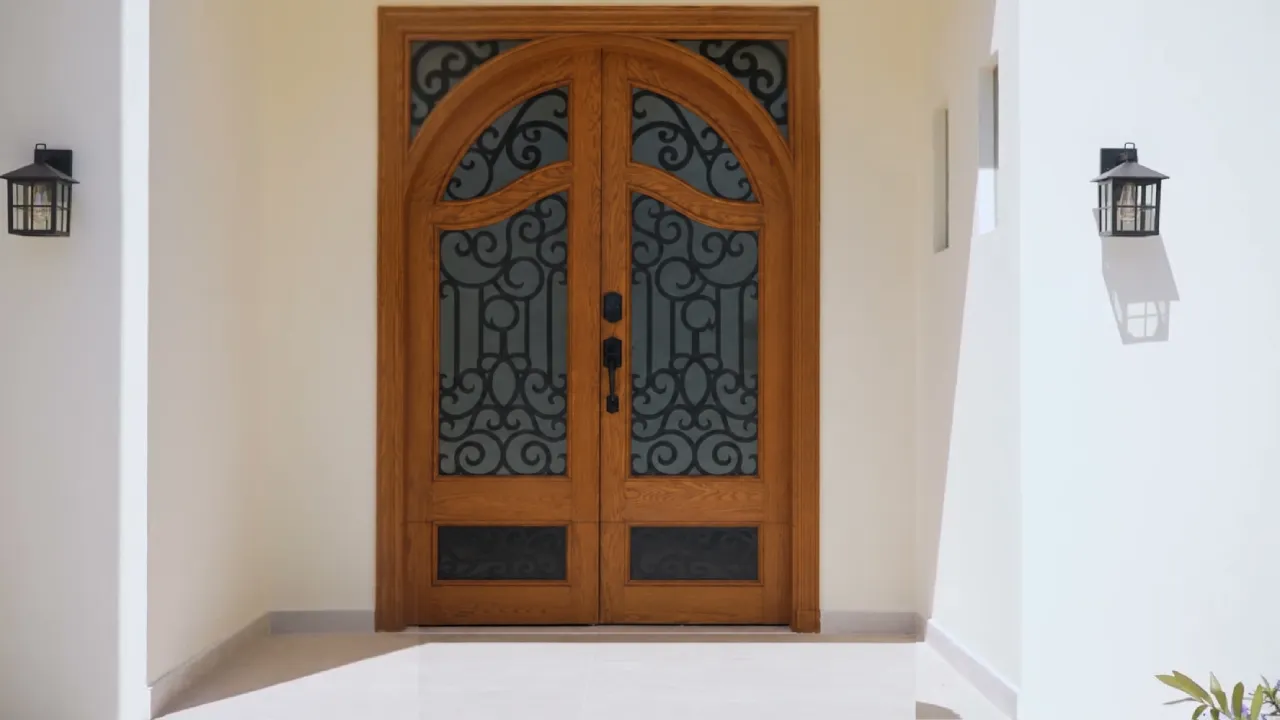 House facade renovation in Meadows Dubai with arched wood entrance door, glass panels, black metal detailing, and exterior wall lanterns.