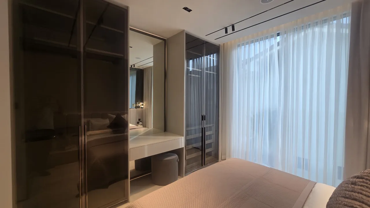 Modern bedroom dressing area with smoked glass wardrobes, mirror panels, vanity desk, sheer curtains and warm neutral bedroom palette