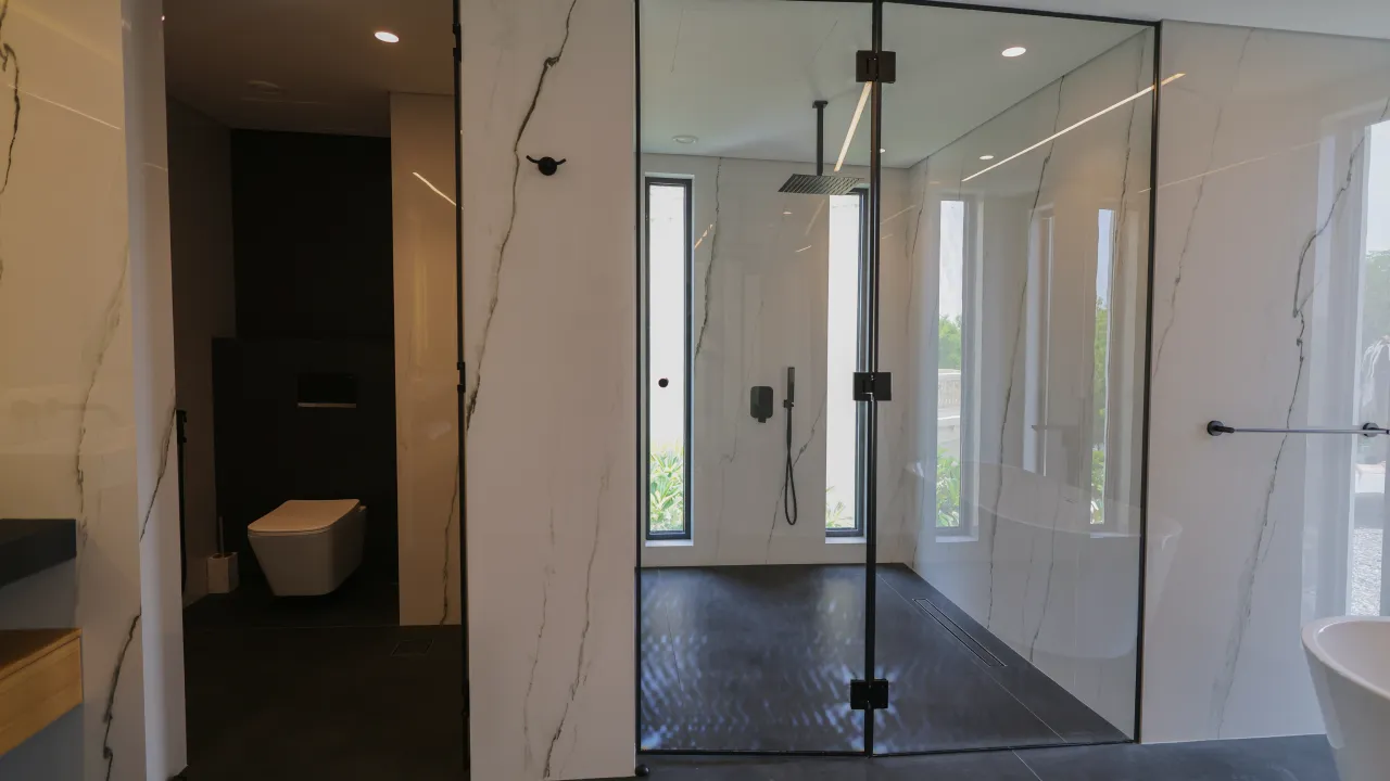 Modern master bathroom renovation with glass shower enclosure, marble-effect wall panels, black fixtures, dark floor, and freestanding bathtub