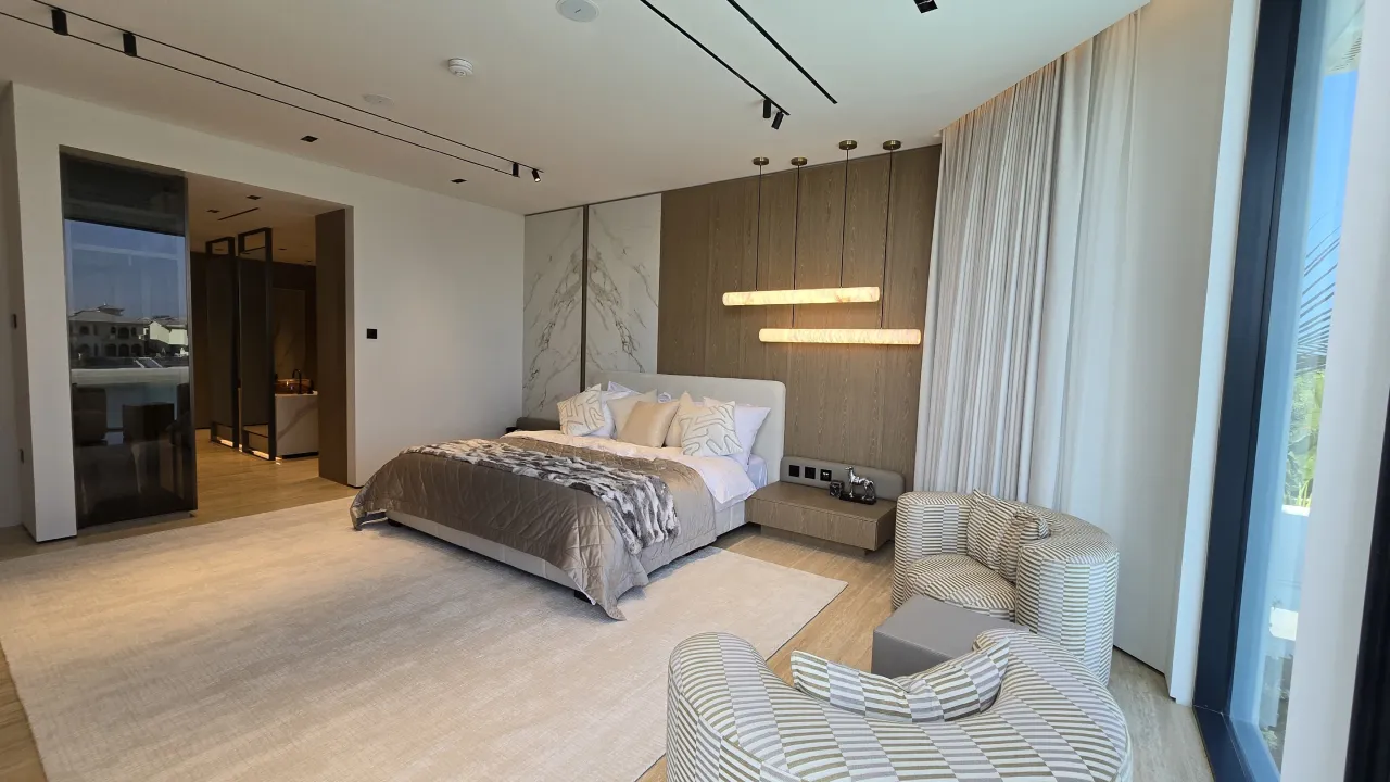 A luxury waterfront master suite redesigned with warm wood detailing, a custom bed wall, and soft seating by the view.