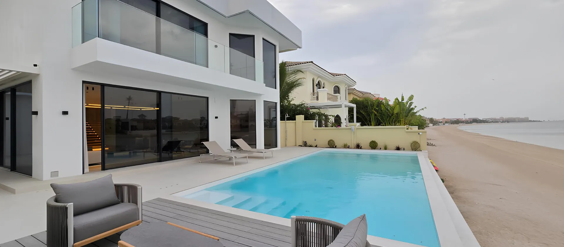 Modern Palm Jumeirah villa exterior renovation with white facade, glass balcony, swimming pool, large windows and outdoor lounge area