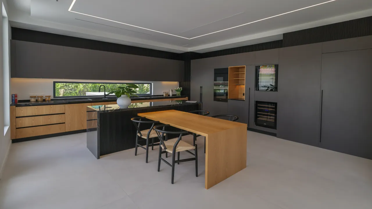 Modern renovated villa kitchen with matte black cabinetry, natural wood details, ribbed island, dining table, and garden-facing window