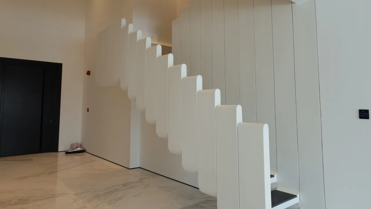 Modern staircase design in a Palm Jumeirah villa renovation with white rounded side panels, black treads, and a sculptural wall treatment