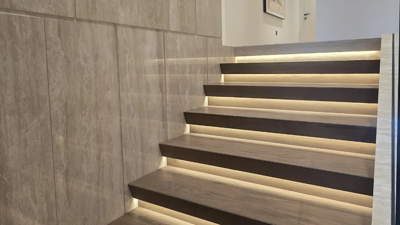 Modern staircase renovation with warm wood treads, textured stone wall cladding, glass railing and concealed step lighting