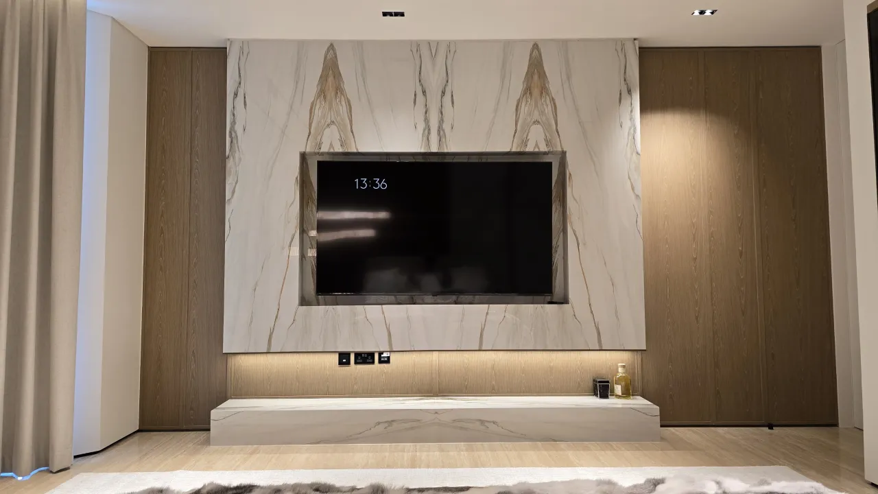 Modern renovation with marble slab TV wall, warm wood side panels, low stone console and soft lighting for a luxury bedroom interior
