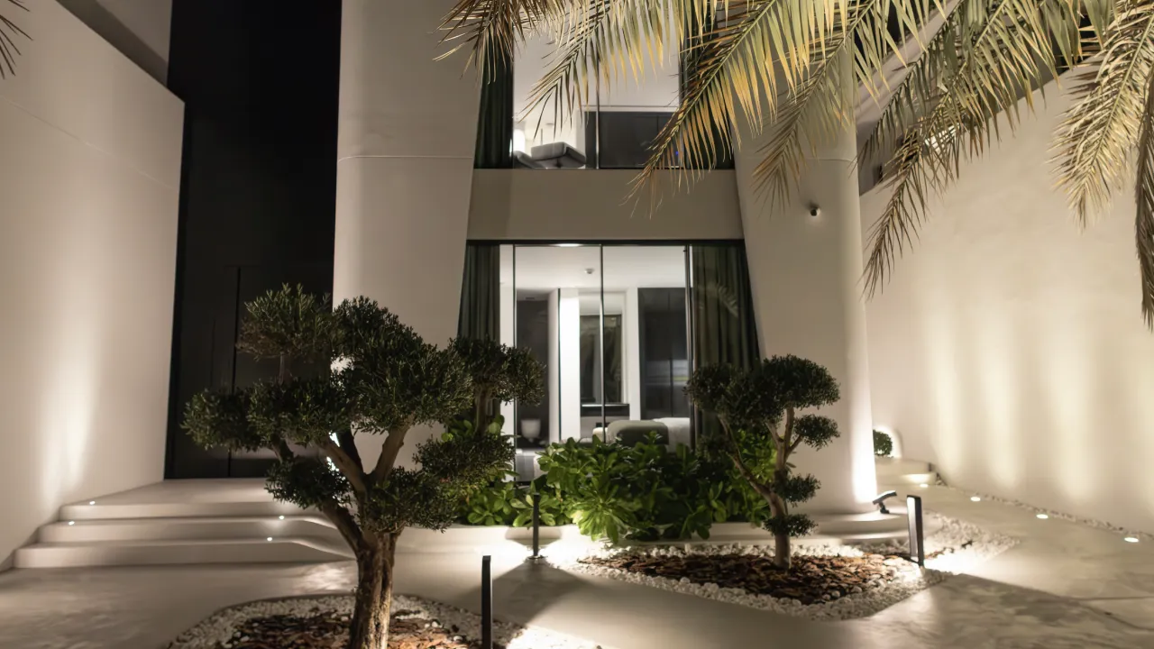 Modern villa landscape lighting after renovation in Dubai with sculptural trees, white walls, stone beds, and warm exterior illumination