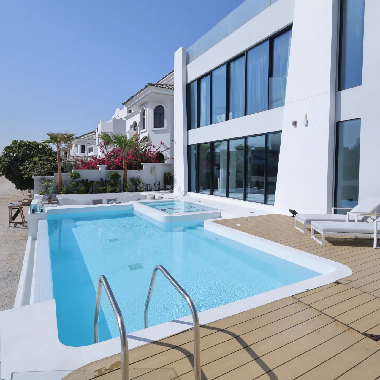 Modern villa pool makeover with pale pool deck, white coping, spa area, glass doors, and timber-look decking