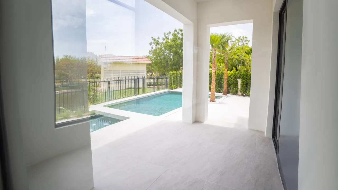 Modern Dubai villa pool terrace with covered patio, large glazing, pale stone paving, palms, and private garden views