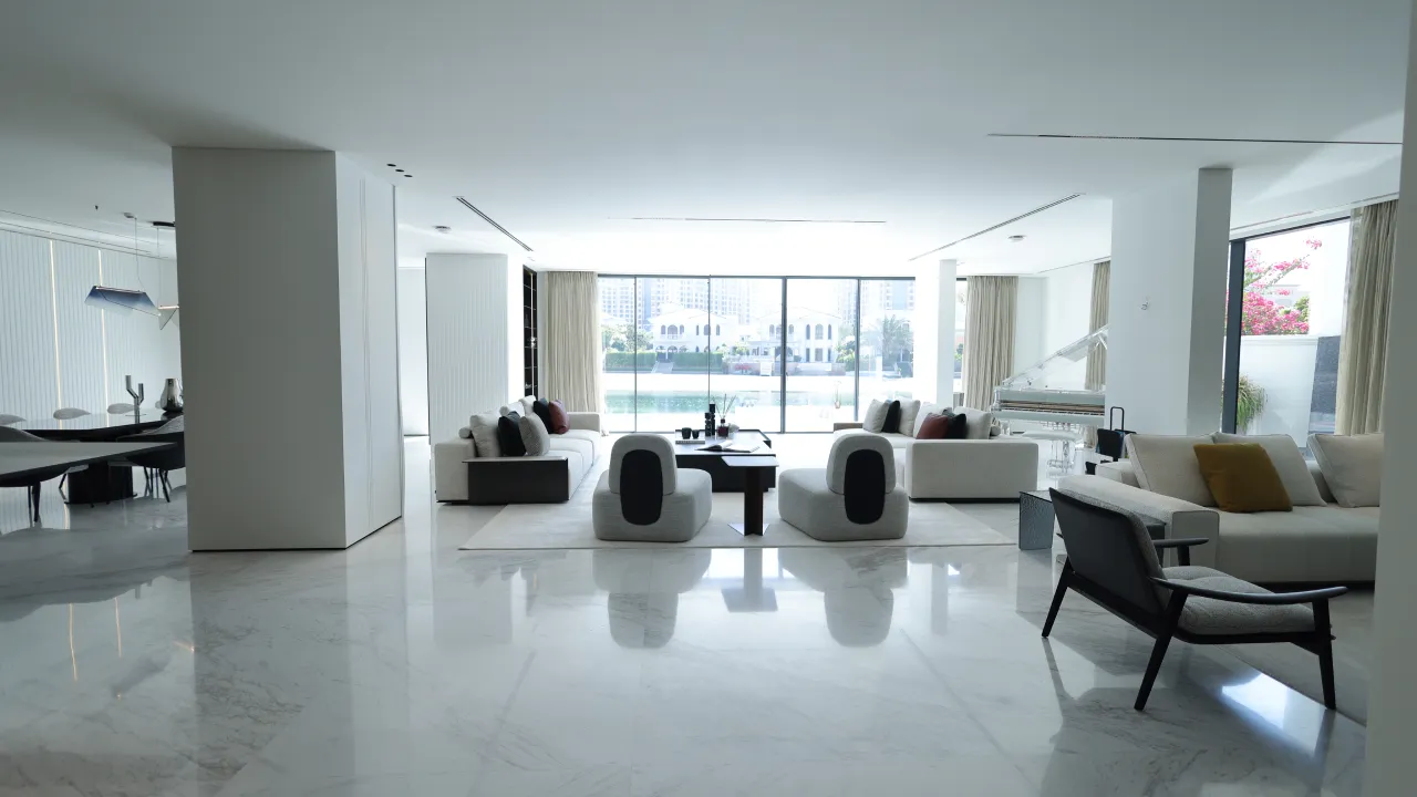 Open-plan living room in a renovated Palm Jumeirah villa with marble-look flooring, pale sofas, large windows, and waterfront views