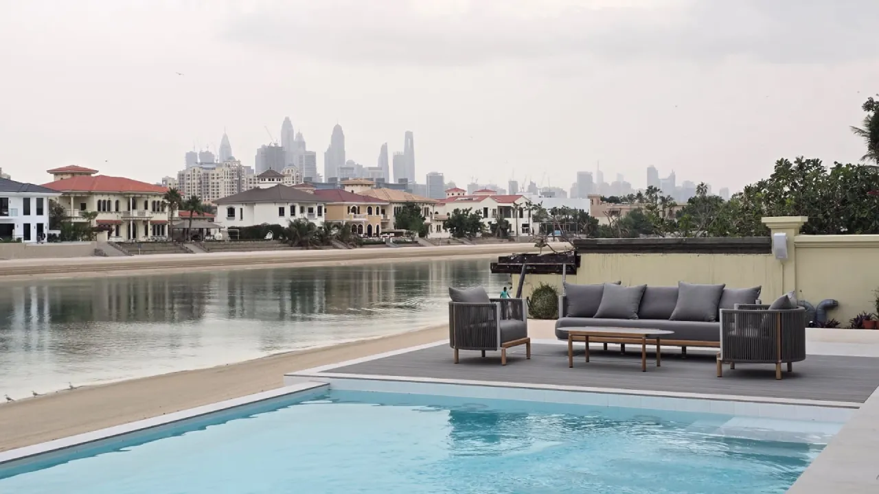 Palm Jumeirah pool lounge after old house renovation with waterfront seating, grey outdoor furniture, swimming pool and Dubai skyline view