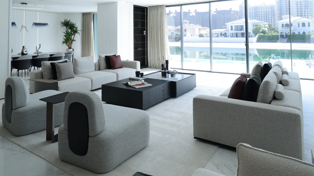 Palm Jumeirah villa living room after renovation with soft neutral seating, black coffee table, dining area, and wide waterfront glazing