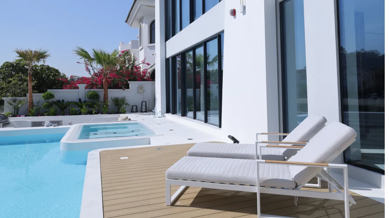 Pool deck renovation with white sun loungers, timber-look deck, large swimming pool, spa zone, and modern villa exterior