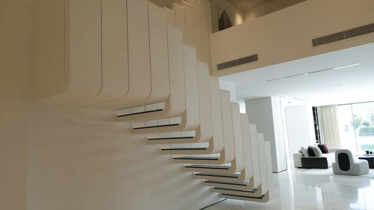 Sculptural white staircase in a modern Palm Jumeirah villa with repeated rounded panels, black step edges, and open living space beyond