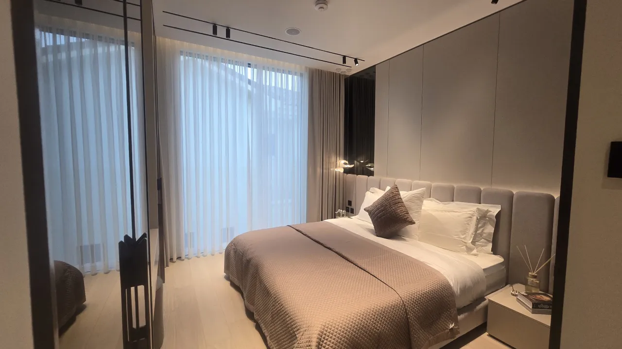 Soft neutral bedroom renovation with padded headboard wall, taupe bedding, sheer curtains, warm bedside lighting and modern wardrobe finish