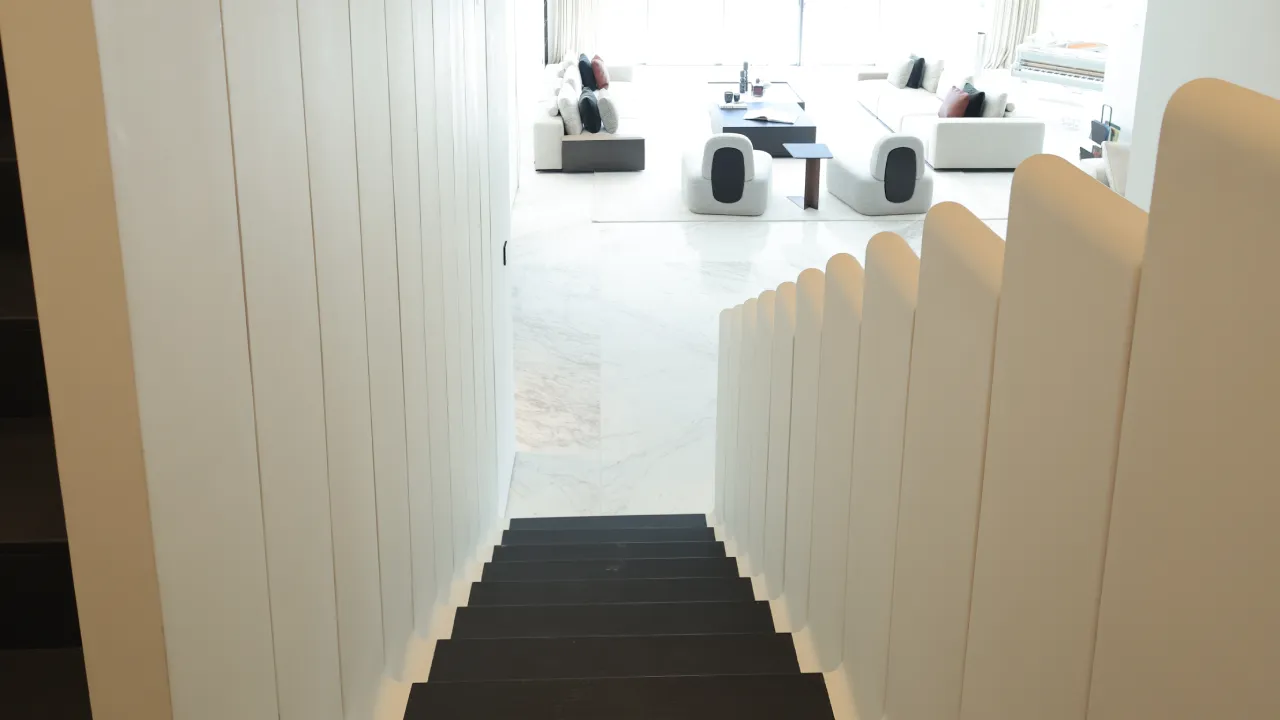 Staircase view toward the living room in a Dubai Palm house after renovation, showing white side panels, dark steps, and bright open interiors
