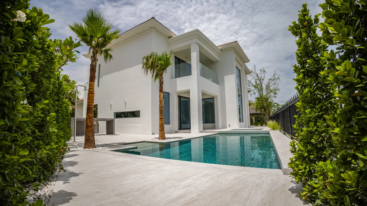 Villa swimming pool restoration with white facade, pale stone pool deck, palm trees, garden hedges, and dark green-blue water