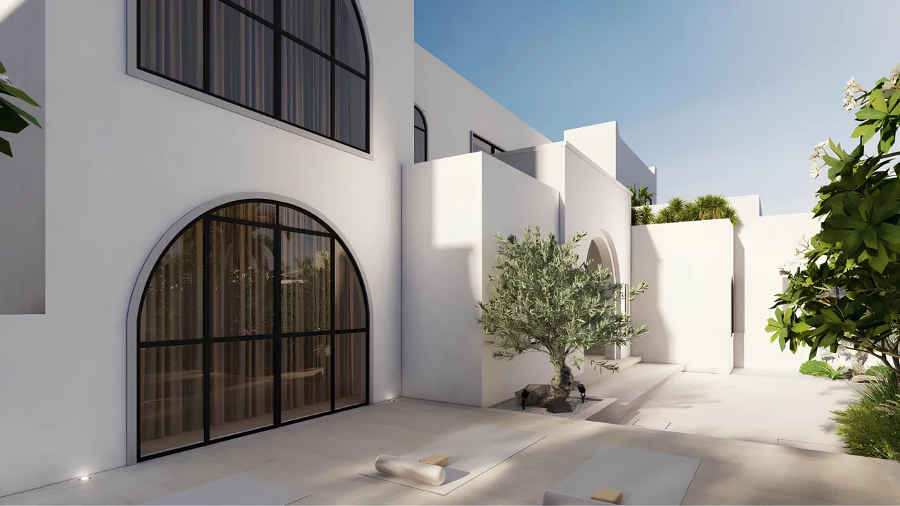 Modern Mediterranean side facade with white walls, arched windows, olive tree, pale terrace flooring, outdoor yoga mats, soft planting, and private garden setting.