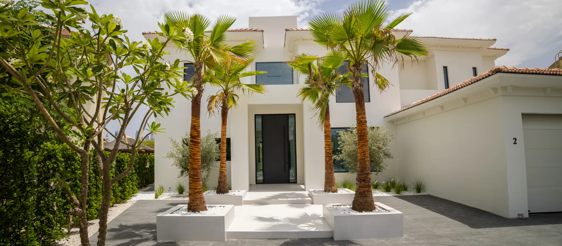 Modern white townhouse construction in Dubai with a tall entrance, palm landscaping, large windows, and an attached garage