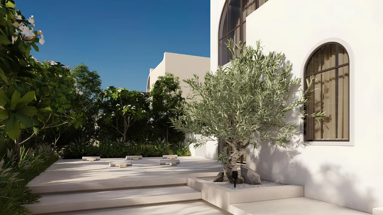 Outdoor yoga area beside a white Mediterranean villa with arched windows, olive tree, pale stone terrace, soft garden planting, and shaded private outdoor space.