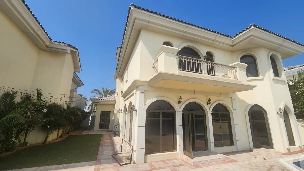 Rear exterior of a Palm Jumeirah villa before renovation with arched doors, metal balcony railing and tiled roof