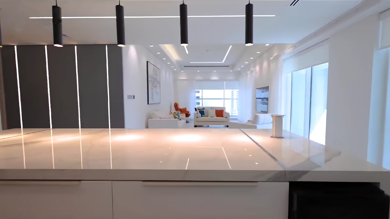 Kitchen island and illuminated grey wall panels leading to the bright family lounge in the renovated Dubai Marina apartment