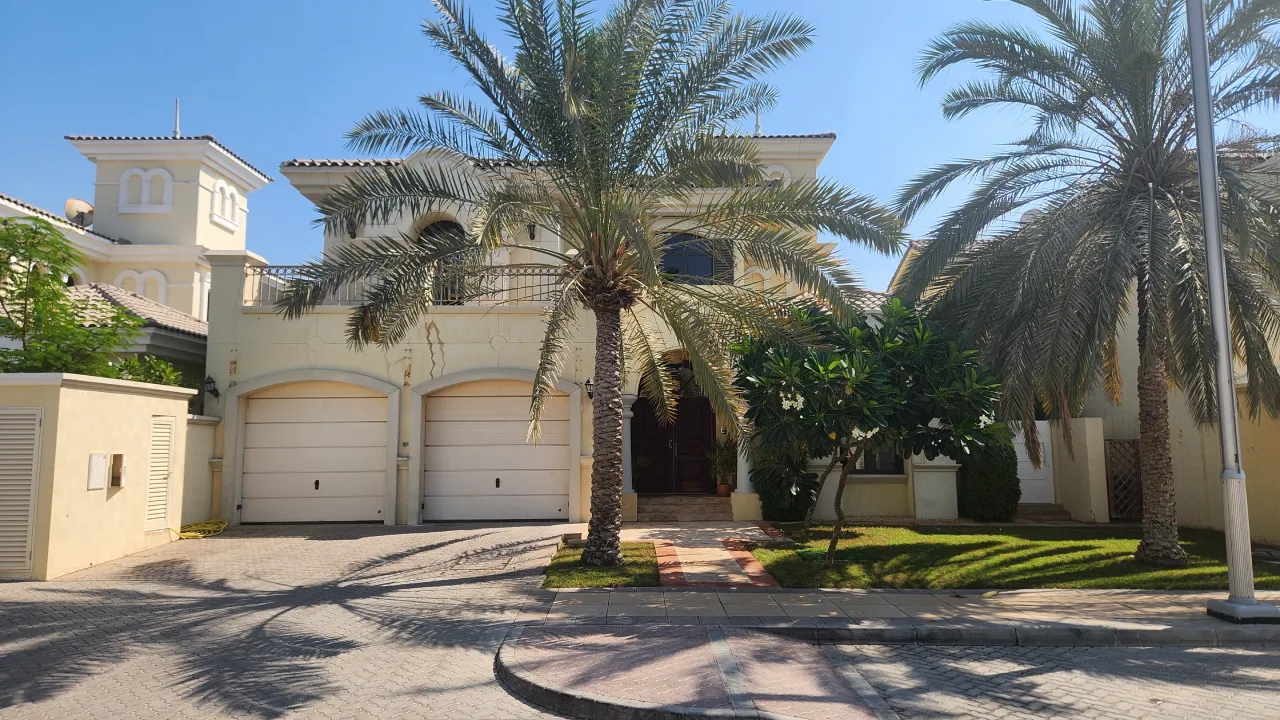 Traditional Palm Jumeirah villa front exterior before renovation with arched garage doors, tiled roofs and mature palm trees