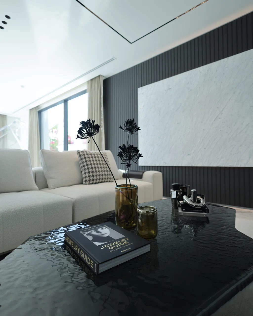 Luxury coffee table detail with black textured top, fashion book, amber glass vessels, white orchids, cream sofa, marble TV wall, and fluted paneling
