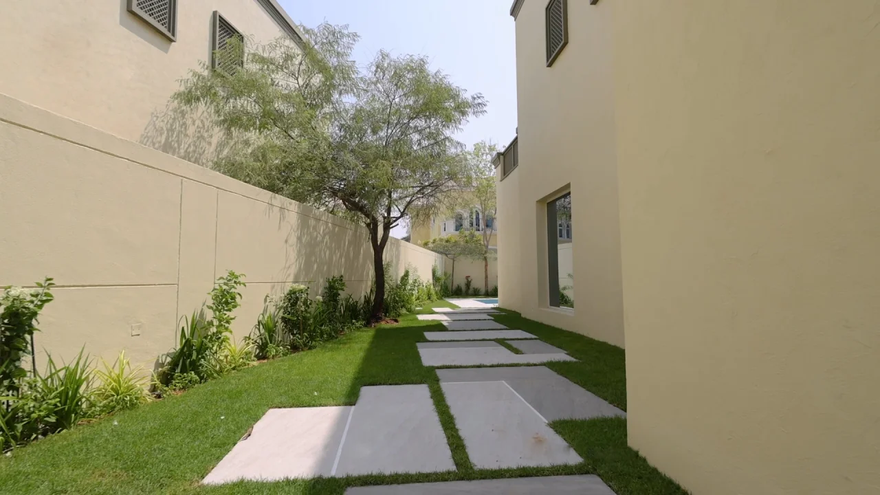 Landscaped side garden with large stepping stones, grass and mature trees beside a upgraded Jumeirah Park villa