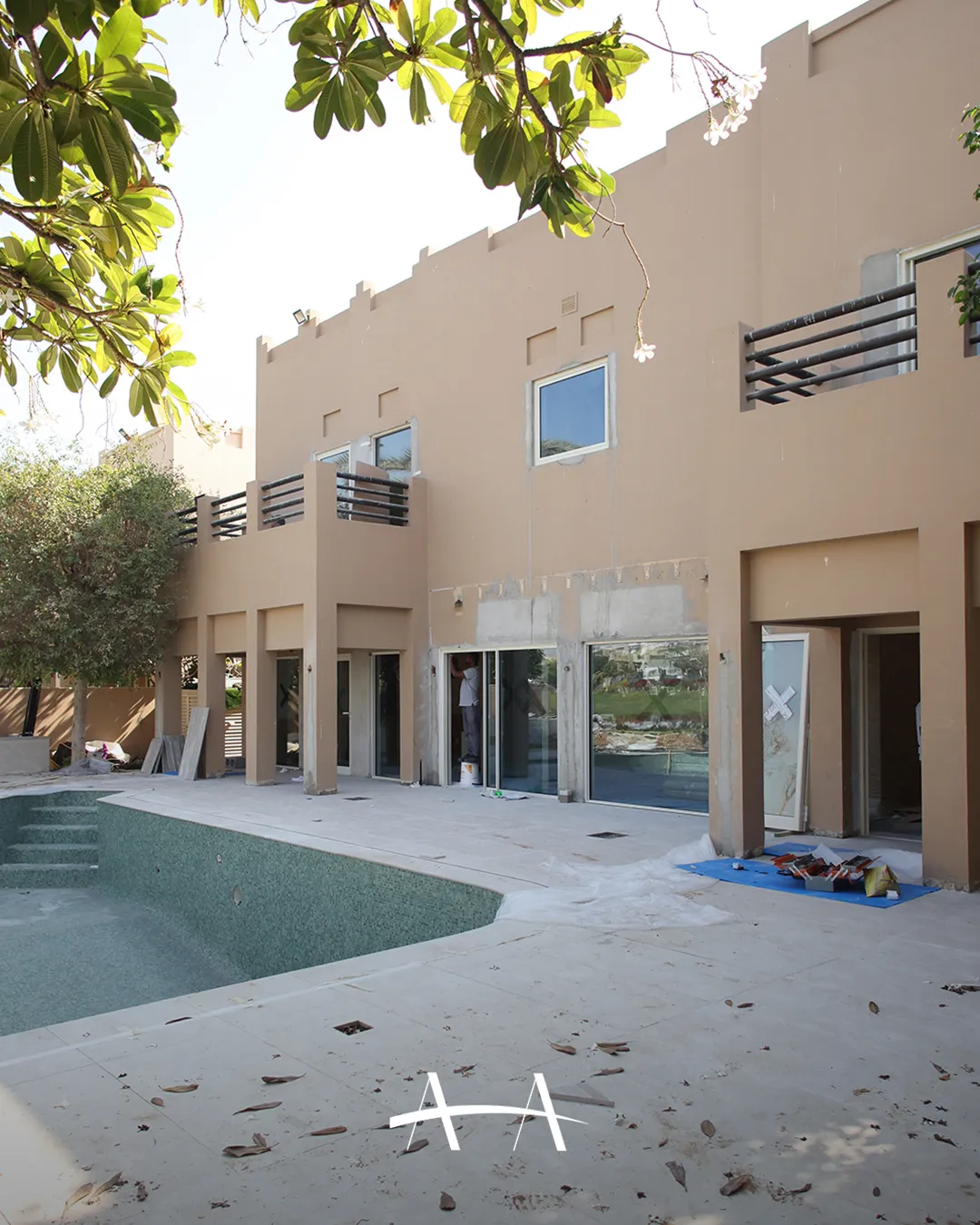 Opposite view of a Meadows villa poolside elevation during facade repairs with an empty pool, unfinished openings and construction materials.