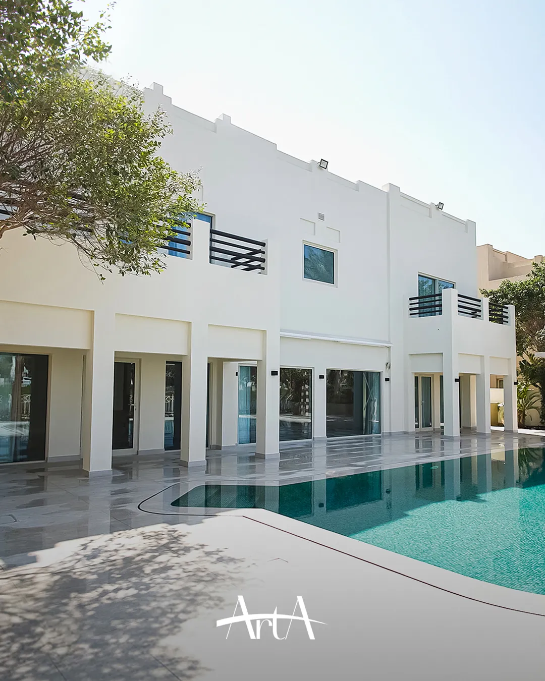Completed Meadows villa rear facade with white exterior finish, black wall lights, pale terrace paving and a filled curved swimming pool.
