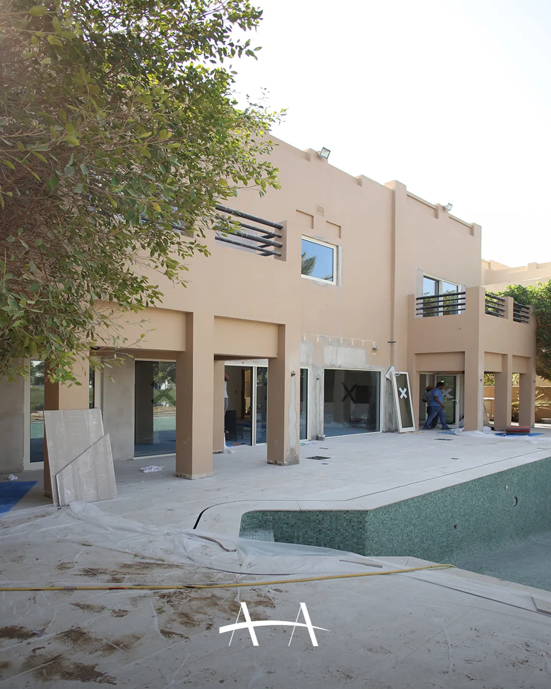 Rear facade of a Meadows villa during renovation with unfinished wall repairs, an empty curved swimming pool and terrace works in progress.