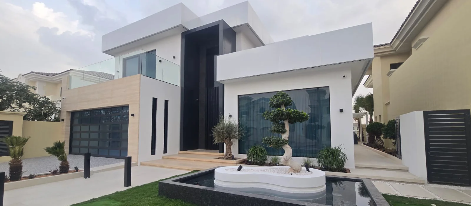 Modern Palm Jumeirah villa facade after renovation with flat rooflines, large glazing, stone cladding, black entrance detailing and landscaped front garden.