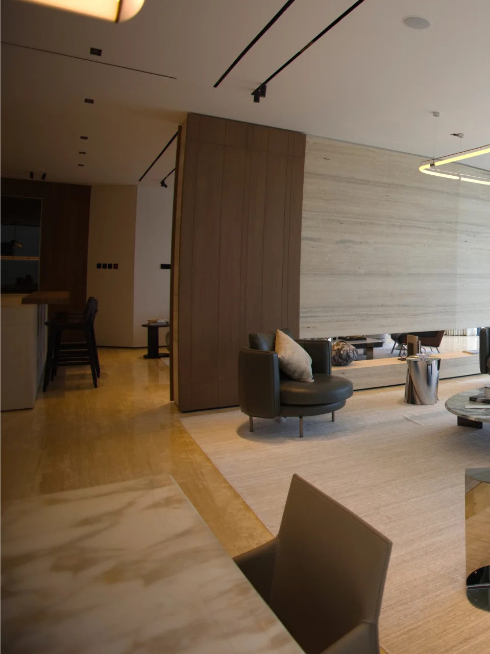 Open-plan Palm Jumeirah living room with stone TV wall, warm wood partition, dark bar area, cream sofa, loop ceiling light, and marble flooring