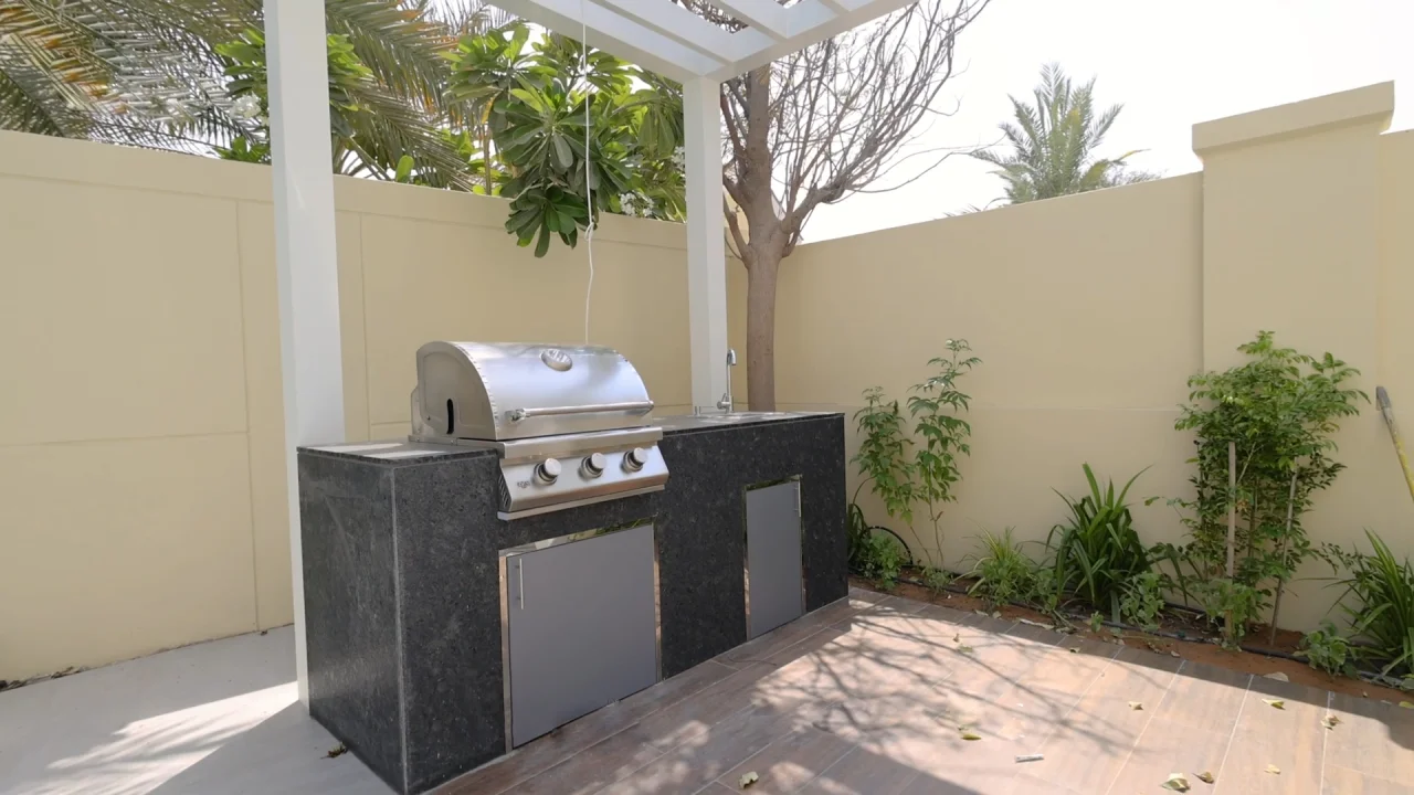 Built-in outdoor kitchen with stainless-steel barbecue, sink and dark stone counter under a white pergola