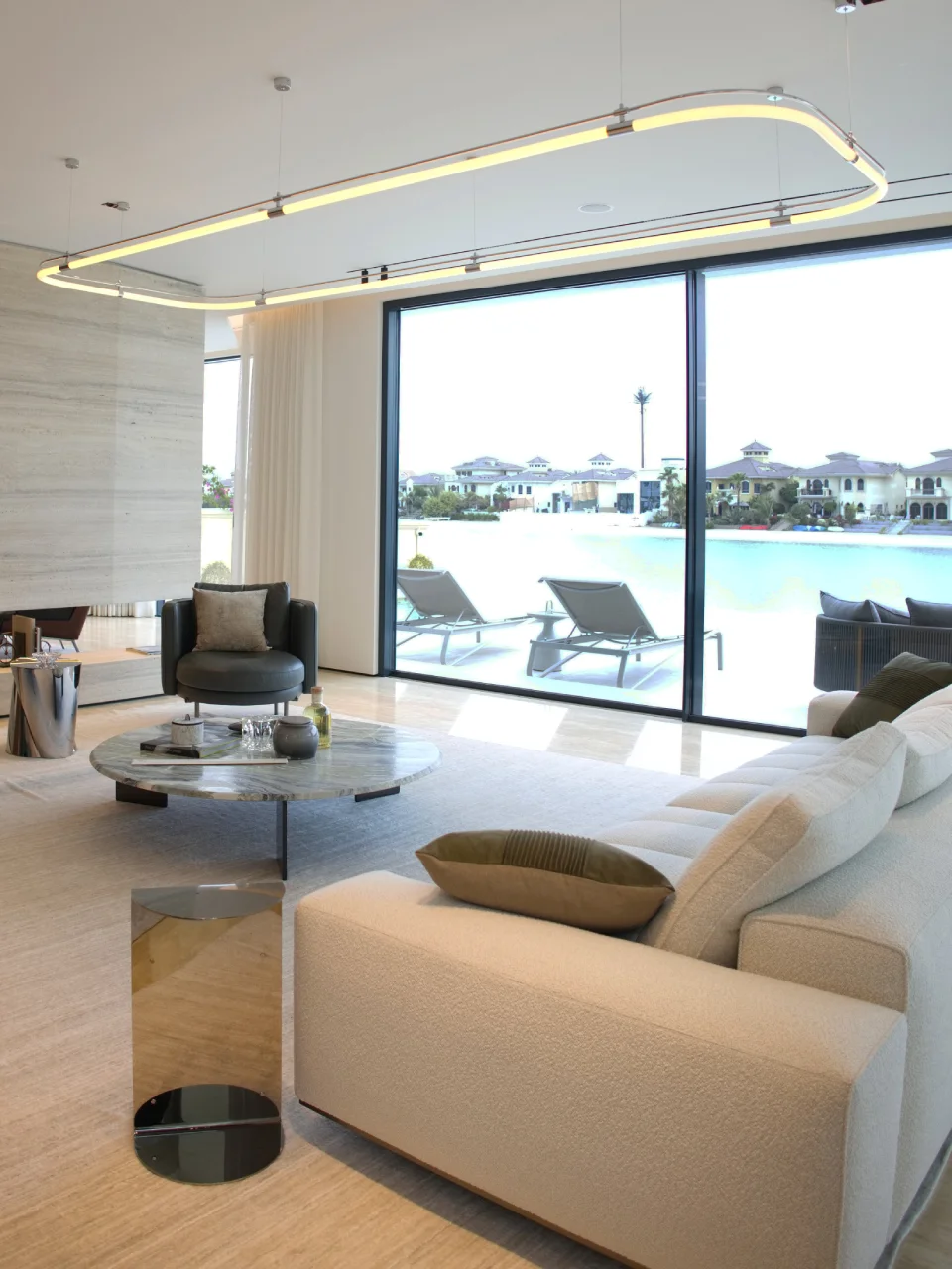 Palm Jumeirah Beachfront villa lounge with curved cream sofa, round marble coffee table, sculptural loop ceiling light, dark lounge chair, and terrace view