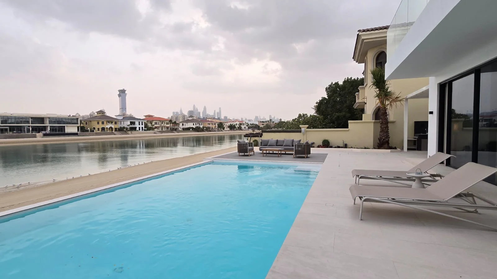 Completed Palm Jumeirah beachfront pool with long water surface, pale stone terrace, sun loungers and waterfront seating