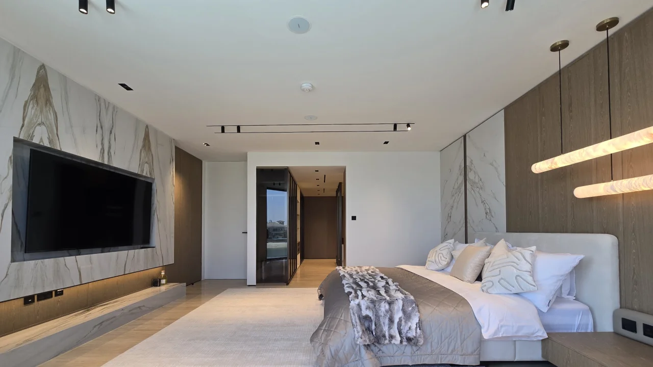 Bedroom After Renovation with Walk-In Dressing Master bedroom after renovation showing the timber bed wall, marble-look media wall and smoked-glass walk-in dressing entrance