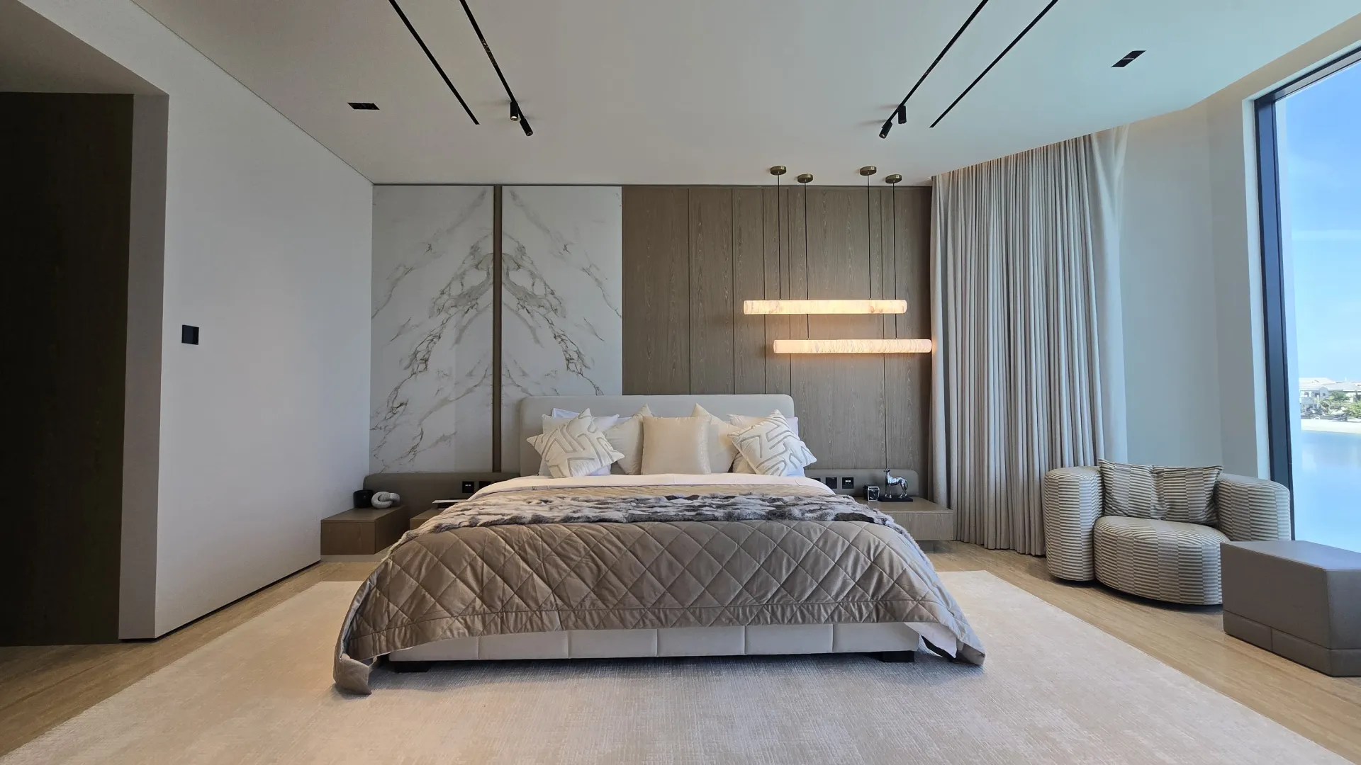 Completed Palm Jumeirah Master Bedroom Completed waterfront master bedroom with timber and marble-look wall panels, suspended horizontal lights and full-height curtains